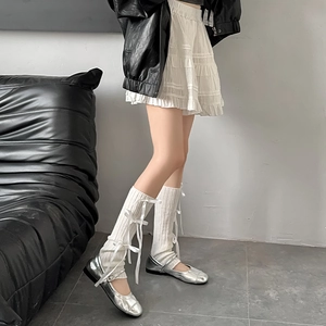 Detail of white knitted leg warmers with bows paired with silver Mary Jane shoes