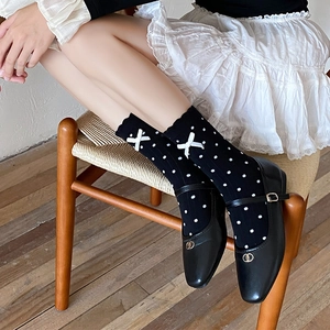 Detail of black polka dot socks with white bows and black Mary Jane leather shoes