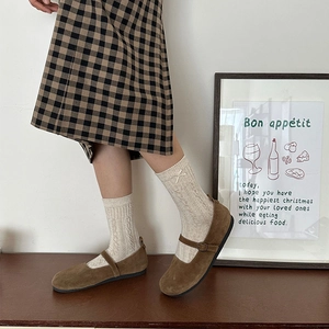 Brown suede Mary Jane shoes paired with white knit bow socks and a plaid skirt