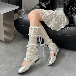 Close-up of white knitted leg warmers featuring elegant satin ribbon bow details