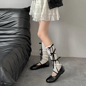 Detail of white ribbed leg warmers with black satin bows and ballet flat shoes