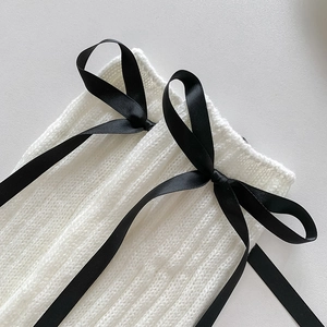 Gros plan sur des jambières en tricot blanc avec des nœuds décoratifs en ruban noir