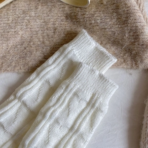 Close-up of white knitted leg warmers with vertical ribbed texture and jacquard patterns