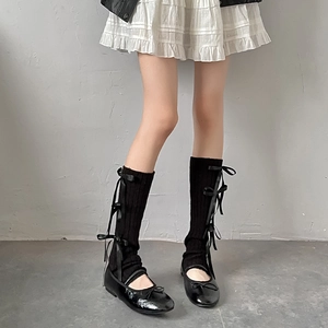 Detail of black knit leg warmers with satin bows and patent leather ballet shoes