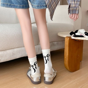 Détail de chaussettes blanches avec nœuds noirs et perles assorties à des baskets argentées