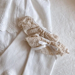 Close-up of white cotton socks featuring delicate lace trim and satin bow accents