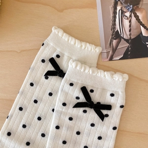 Close-up of white polka dot knit socks featuring a velvet bow and wavy ruffled cuffs