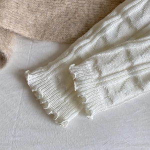 Detail of white cable knit leg warmers with delicate ruffle edges and soft wool texture