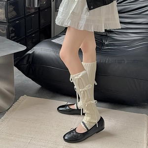 Detail of white knit leg warmers featuring three delicate ribbon bows in balletcore style