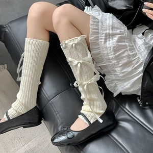 Detail of cream knit leg warmers featuring vertical ribs and four silk bow accents