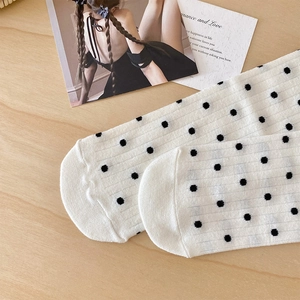 Detail of white knit socks with black polka dots and vertical rib texture on wood