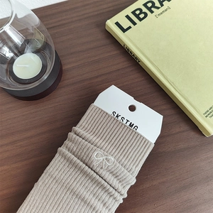 Dettaglio di calze in maglia beige a coste con ricamo a fiocco bianco su fondo di legno