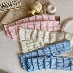 Detail view of knitted leg warmers with diamond texture and ruffled edges in three colors