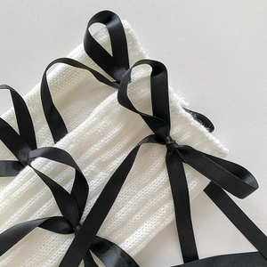 Close-up of ribbed knit leg warmers with black satin ribbon bows and criss-cross straps