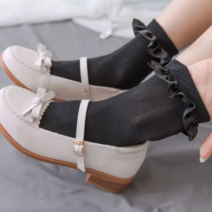 Close-up of white Mary Jane shoes with black mesh lace socks and ruffled satin edges