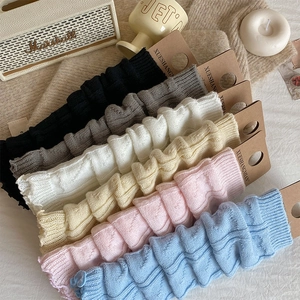 Close-up of assorted cable knit leg warmers in various pastel colors with card packaging