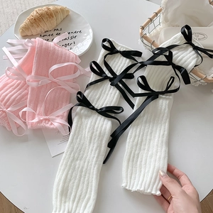 Detail of pink and white cable knit leg warmers featuring decorative satin ribbons