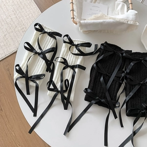 Detail of ribbed knit leg warmers with black satin bows in white and black colors