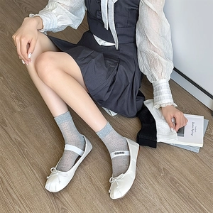 Dettaglio di ballerine Mary Jane bianche con cinturino elastico e calzini grigi a costine