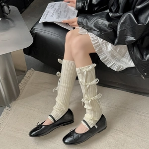 Close-up of cream ribbed leg warmers featuring four elegant satin bows in balletcore style