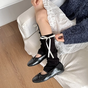 Détail de jambières en tricot noir avec nœuds blancs et ballerines pour un style balletcore
