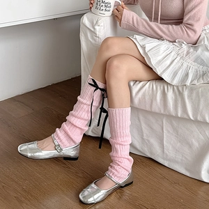 Gros plan sur des jambières en maille rose avec nœuds noirs et chaussures Mary Jane