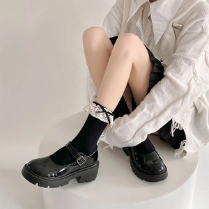 Detail of black Mary Jane shoes with metal buckle and lace bow socks on a white pedestal