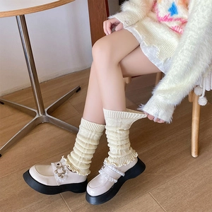 Close-up of cream knitted leg warmers with vertical ribs and wavy edges on mary jane shoes