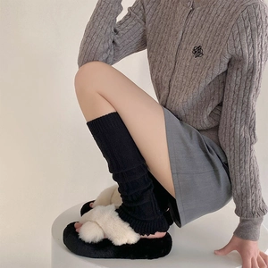 Close-up of stylish black knitted leg warmers paired with plush faux fur cross-band slippers