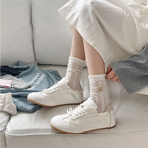 Détail de chaussettes en résille blanche avec broderie ours et baskets blanches