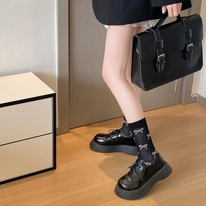 Detail von schwarzen Lackleder-Plateau-Oxfords kombiniert mit rosa Schleifen-Socken