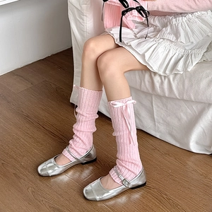 Jambières en tricot rose avec nœuds en ruban portées avec des chaussures Mary Jane