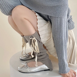 Dettaglio di scaldamuscoli in maglia grigia con nastri panna e ballerine argento