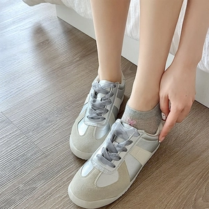 Top view of silver and white leather sneakers with elegant grey ribbon laces on wood floor