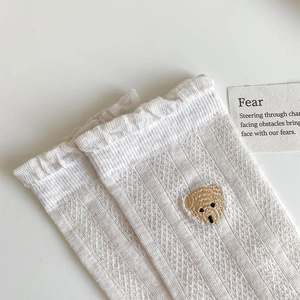 Détail de chaussettes en résille blanche avec broderie d'ours et bords volantés