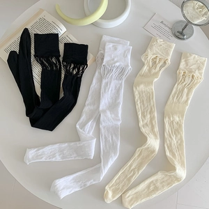 Detailed macro view of mesh cutout thigh-high socks with fringe trim on a white table