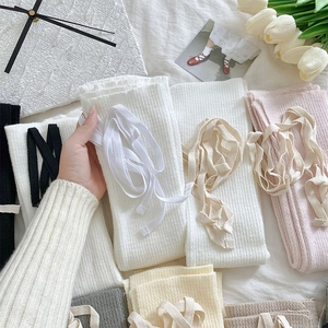 Dettaglio di scaldamuscoli in maglia con nastri in bianco, rosa e varie tonalità