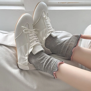 Detail of grey hollow lace socks with pink ruffle edges worn with white leather sneakers