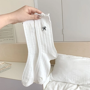 Detailed view of white calf socks with ruffled edges and small black bow embroidery