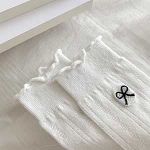 Detailed view of white knit socks with black bow embroidery and ruffled edge design