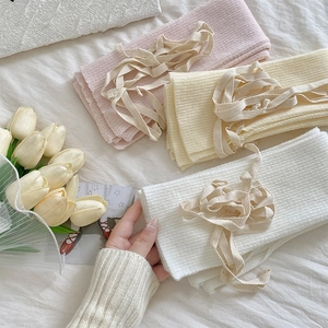 Dettaglio di scaldamuscoli in maglia con nastri e fiocchi rosa, beige e bianchi