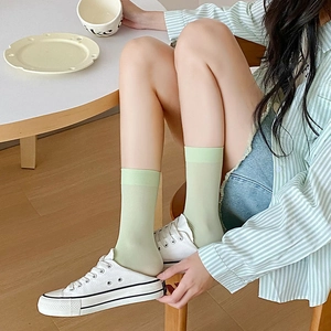 Close-up of light green velvet crew socks with ribbed cuffs worn with white canvas slippers