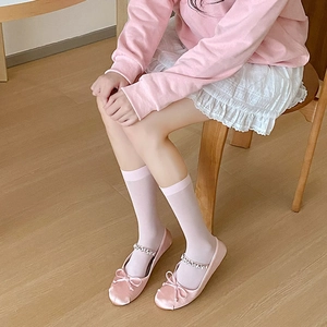 Pink satin ballet flats with rhinestone straps and bow detail shown on white lace socks