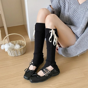 Dettaglio di scaldamuscoli neri in maglia con fiocchi bianchi e scarpe Mary Jane nere