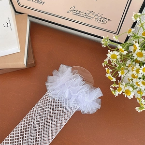 Detail of white fishnet stockings featuring ruffled organza lace on a wooden surface