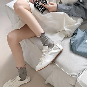 Detail of grey ribbed socks with pink ruffle trim paired with white leather sneakers