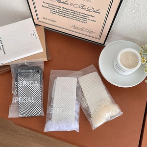 Three pairs of lace-trimmed mesh socks in black, white, and beige on a wooden table
