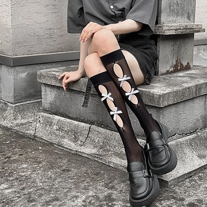 Detail of Lolita style black mesh socks featuring side cut-outs and white ribbon bows