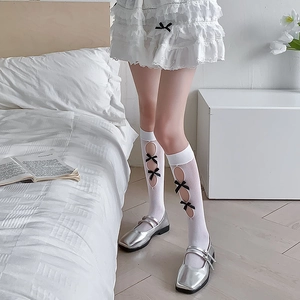 Detail of white hollow-out knee high socks with black satin bows and Mary Jane shoes