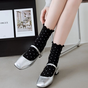 Close-up of black polka dot socks with ruffled edges paired with silver Mary Jane shoes